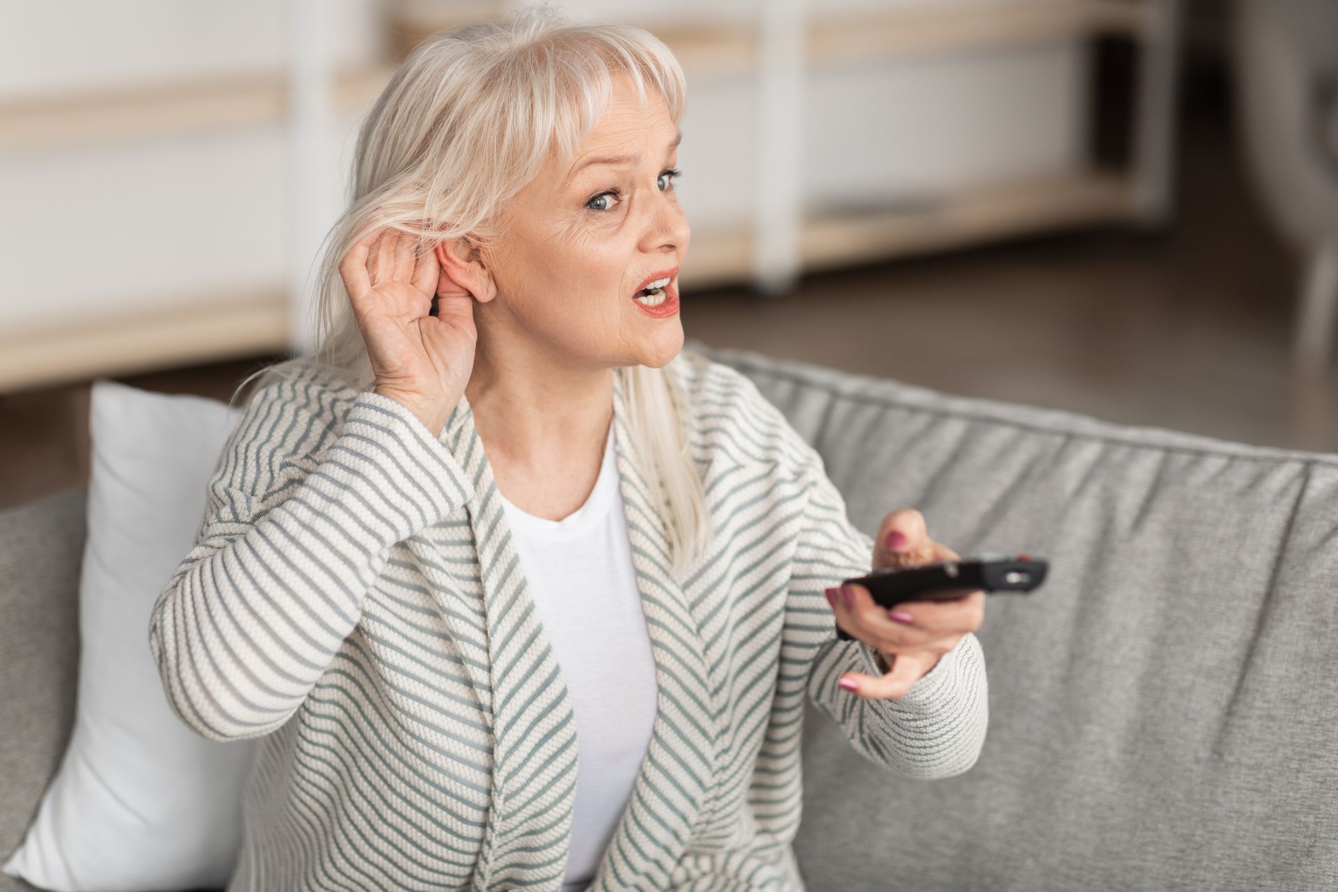 A mature woman holding out her ear while she puts the volume up on a TV remote.
