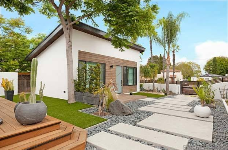 Modern home with a white exterior, wooden accents, and a landscaped yard with stepping stones and greenery.