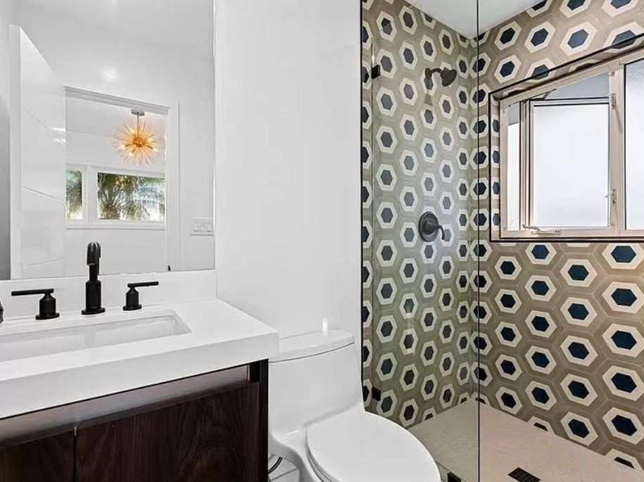 Bathroom with white sink, dark cabinet, patterned shower tile, and window.