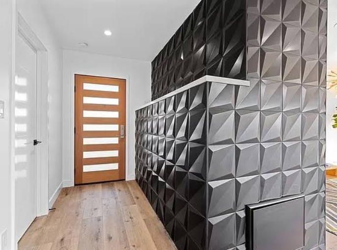 Hallway with wooden floor, door, and textured, geometric black accent wall.