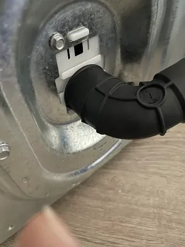 Black drain hose connected to a white plastic bracket on a metal appliance.
