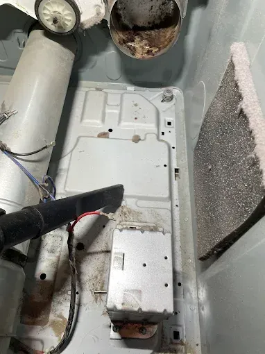 Interior of a dryer with lint and debris; vacuum cleaning.