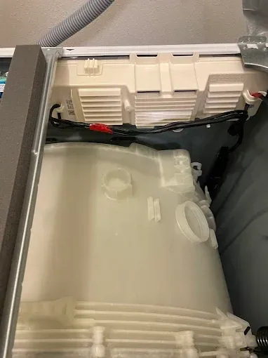 Inside of a washing machine; showing the drum and detergent dispenser, with various hoses and wiring.