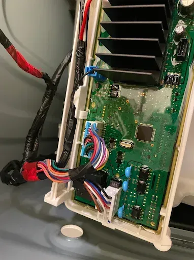 Circuit board with colorful wires and heat sink in a white plastic housing, inside an appliance.