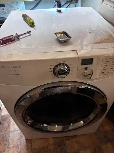 White front-load washing machine with tools on top; being repaired.