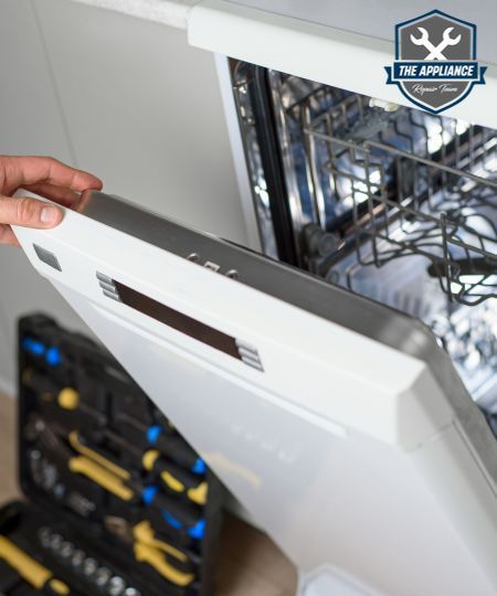 Person opening a white dishwasher door with a toolbox in the foreground.