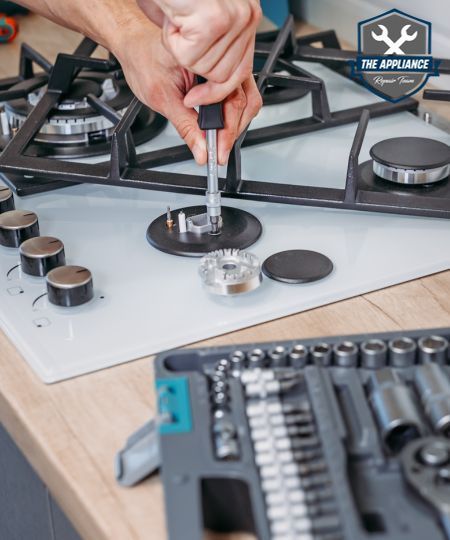 Person repairs a gas stovetop with tools, near knobs and burners.