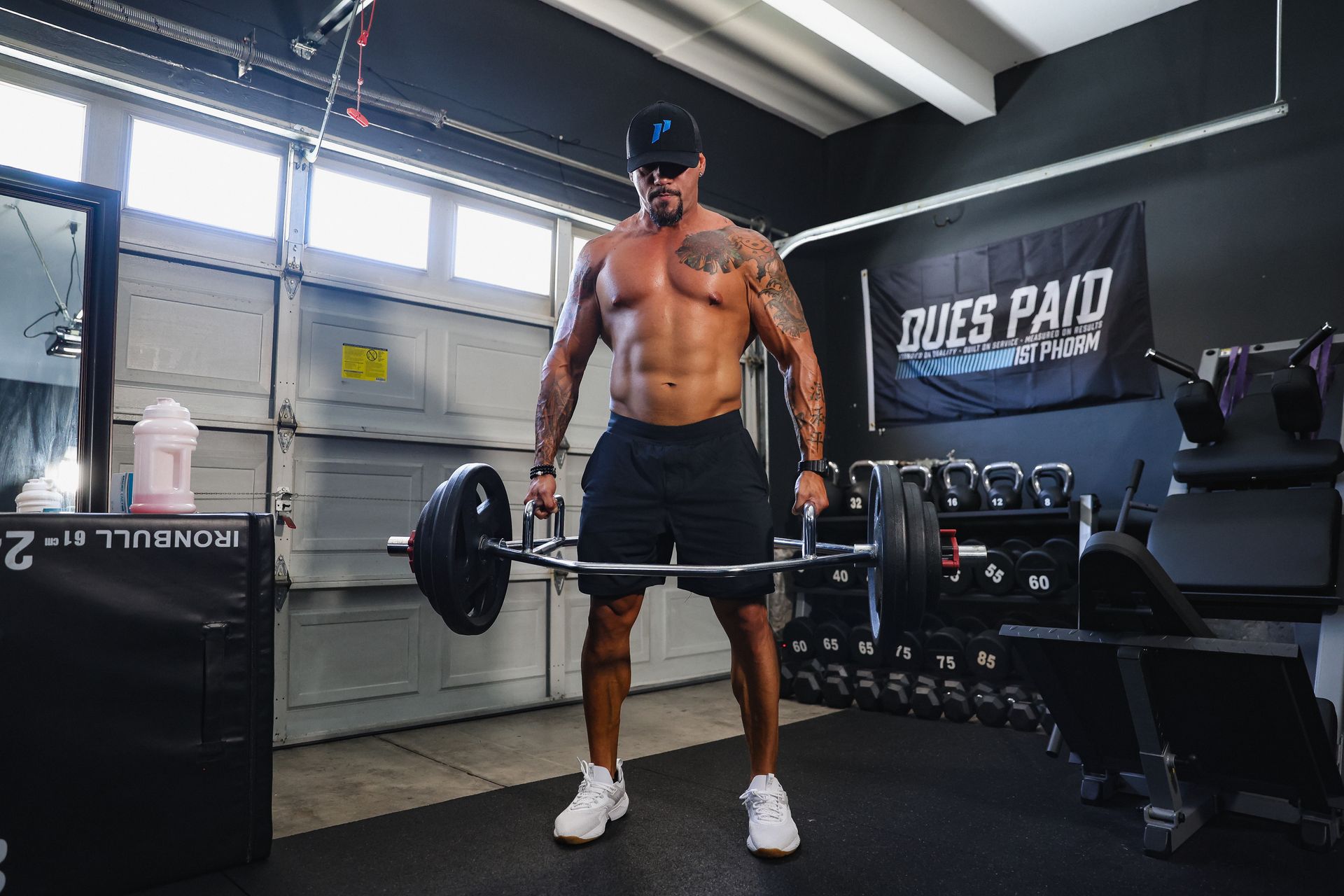A shirtless man is lifting a barbell in a garage.
