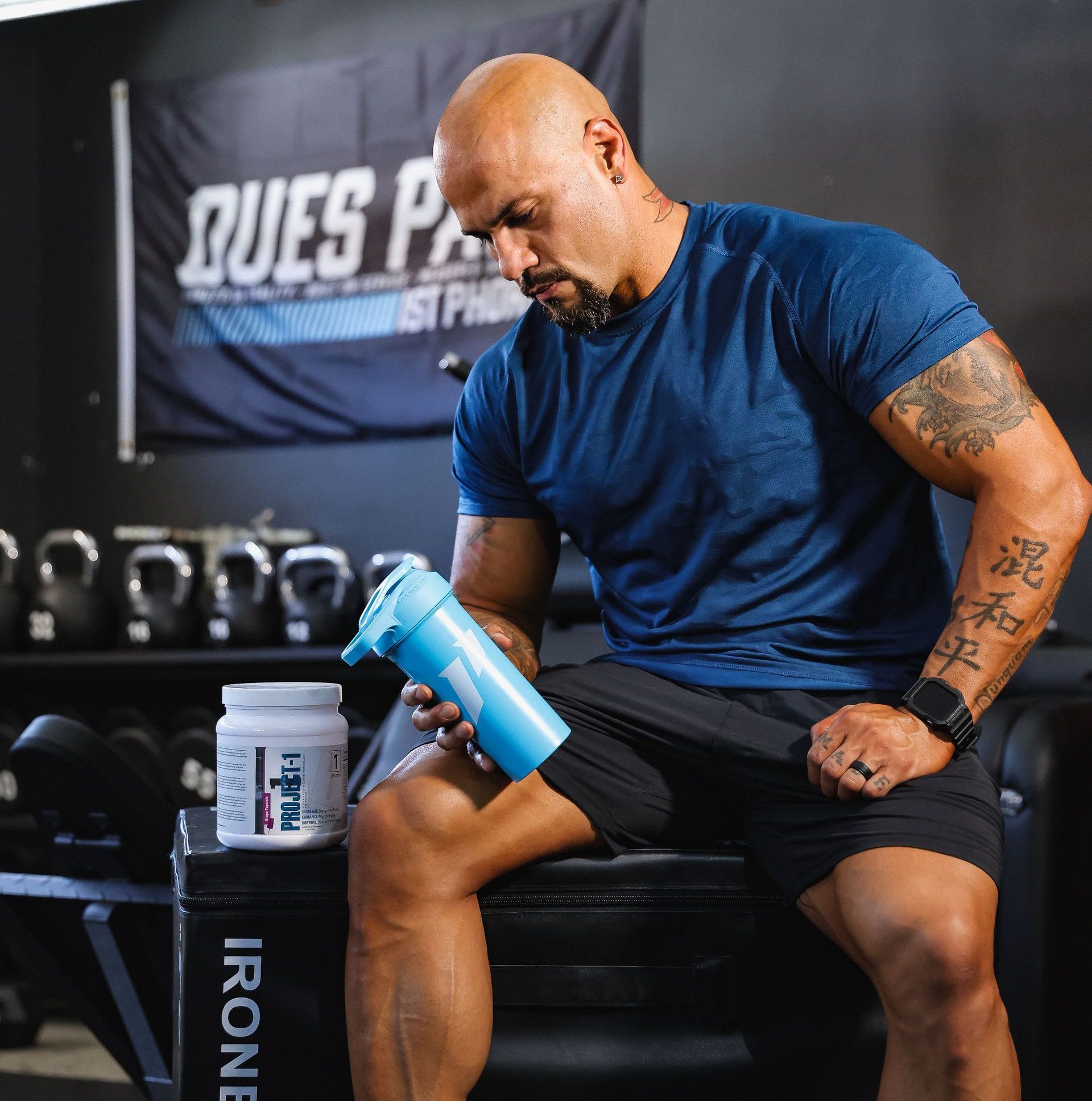 A man is sitting on a bench in a gym holding a blue bottle