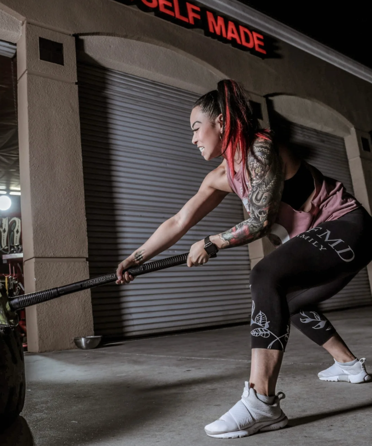 A woman is pushing a tire in front of a building that says self made