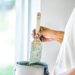 A house painter dips his brush into a can of paint. rr