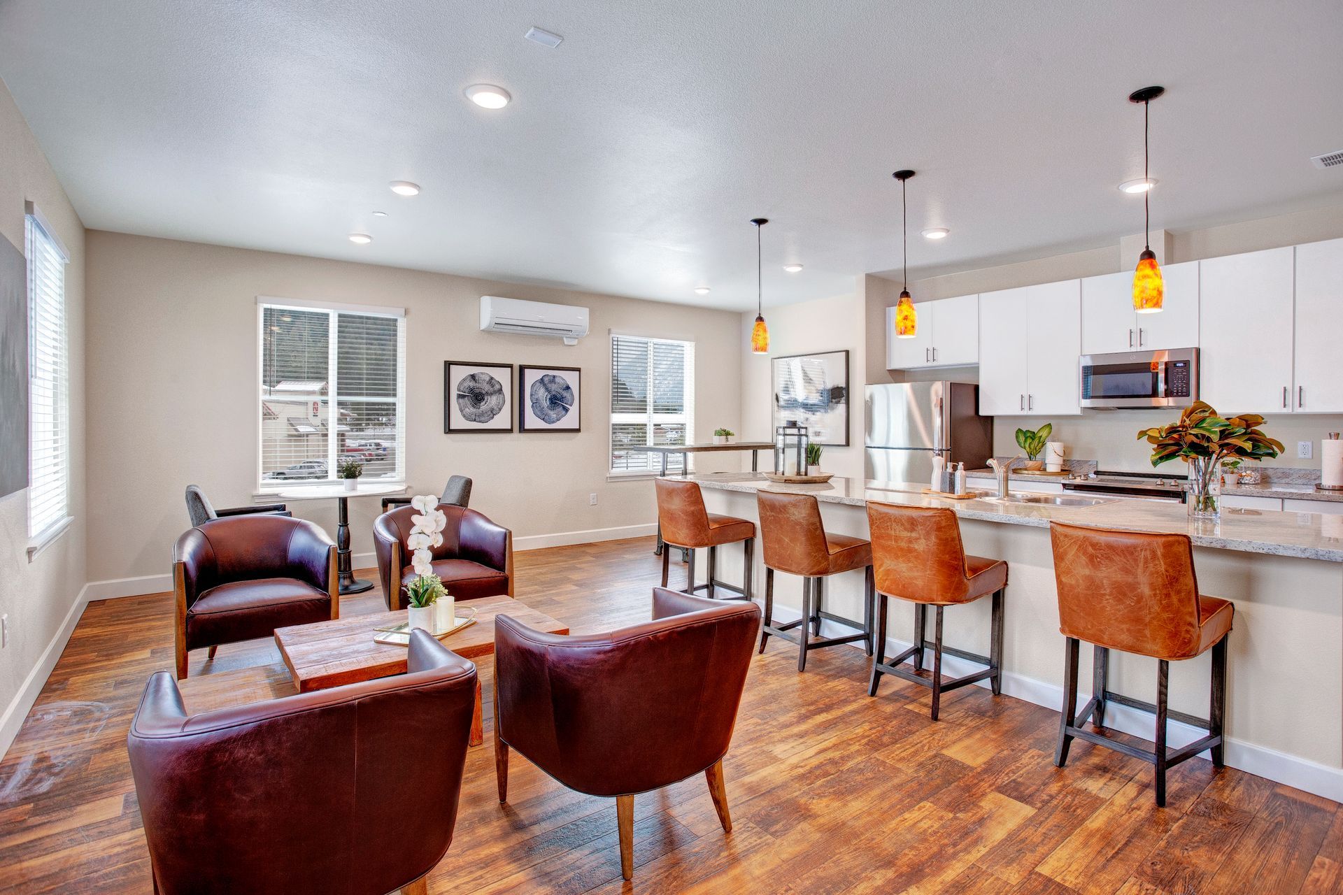 A living room with hardwood floors , chairs , tables and a kitchen.