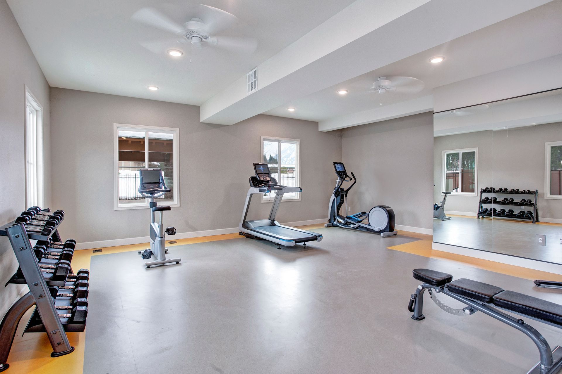 A gym with a treadmill , elliptical , dumbbells and a bench.