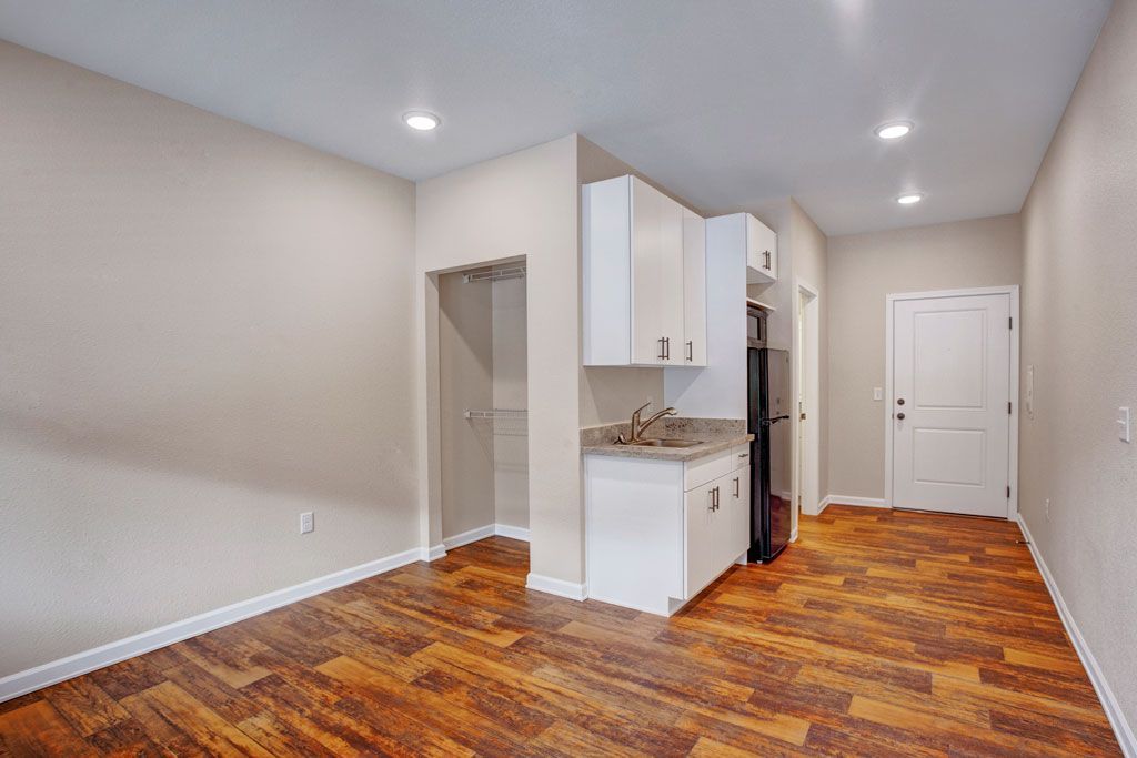 An empty apartment with hardwood floors and white cabinets.