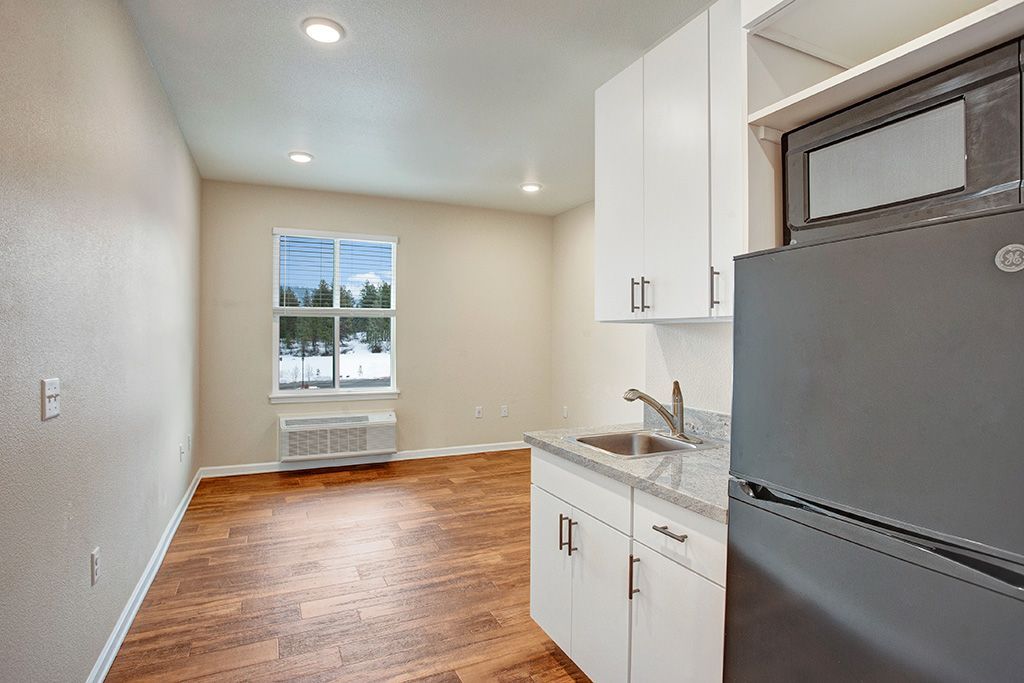 A kitchen with a refrigerator , sink , microwave and window.