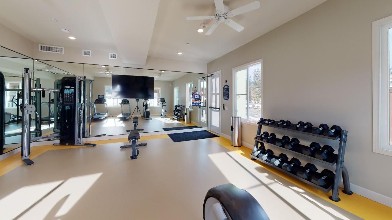 A large gym with a lot of equipment and a ceiling fan.