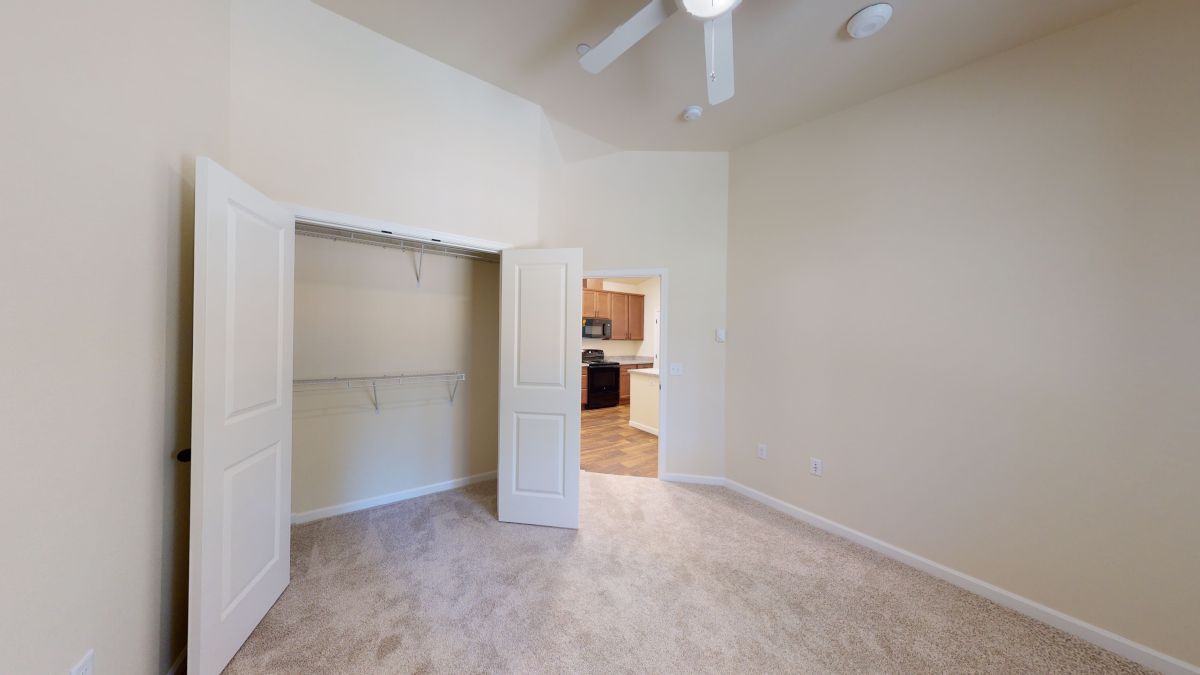 An empty bedroom with a ceiling fan and a closet.