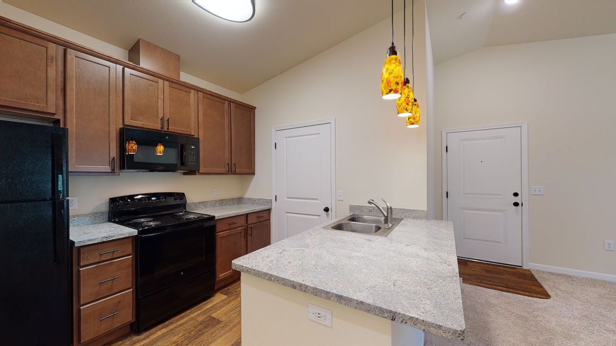 A kitchen with granite counter tops , a black refrigerator , a stove , and a sink.