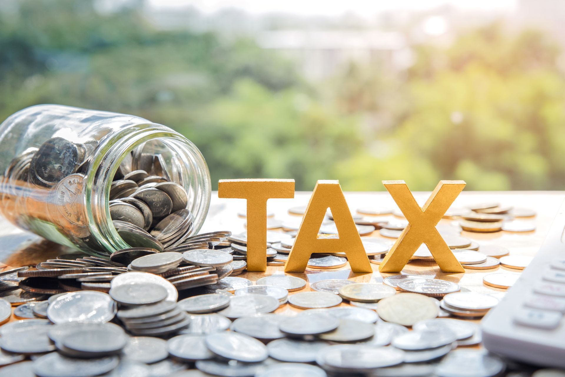 A jar filled with coins next to a pile of coins and the word tax.