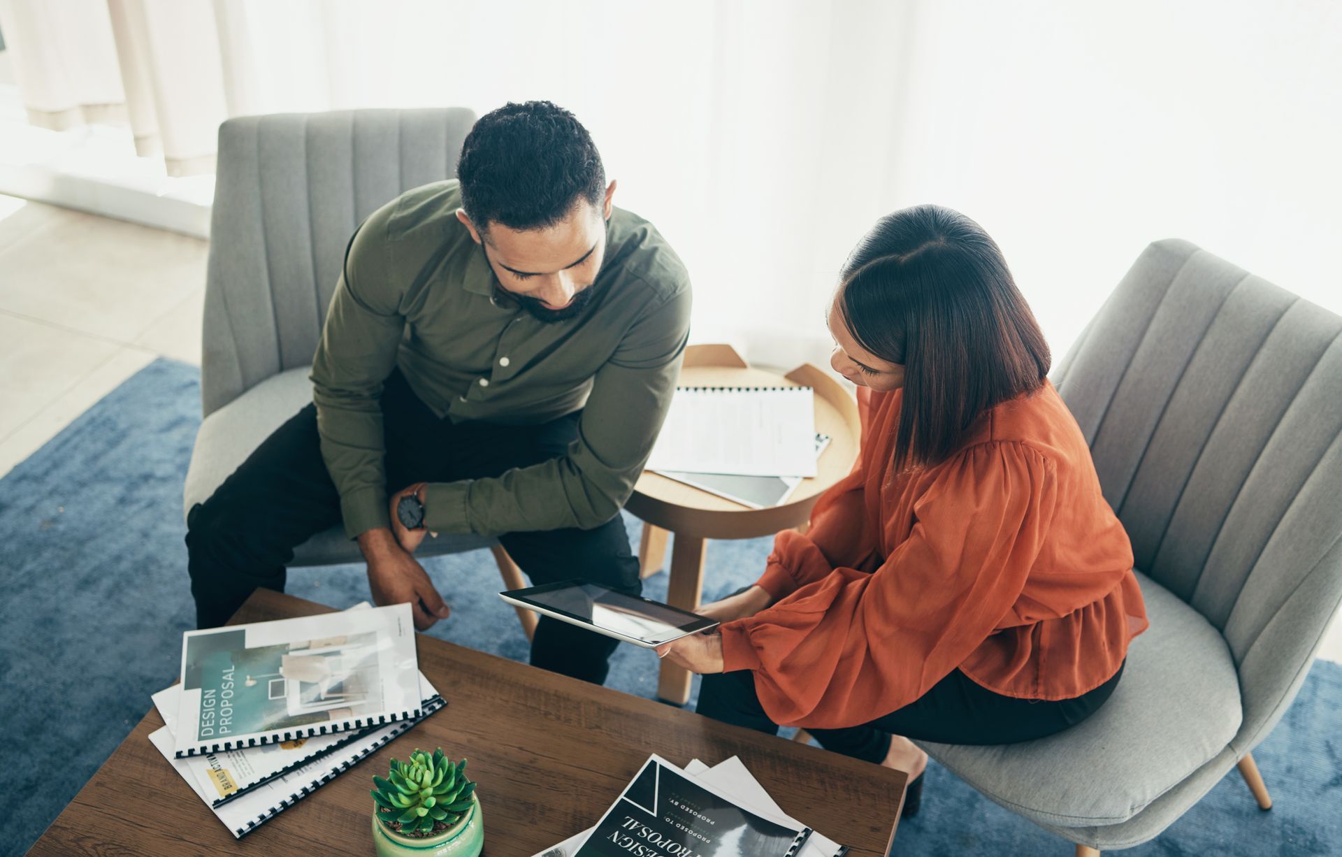 A man and a woman are sitting at a table looking at a tablet.