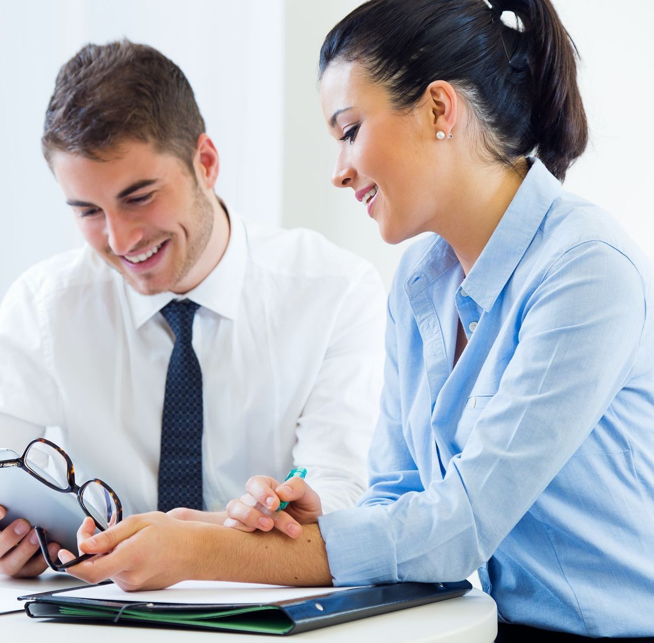 A man and a woman are sitting at a table looking at a tablet.