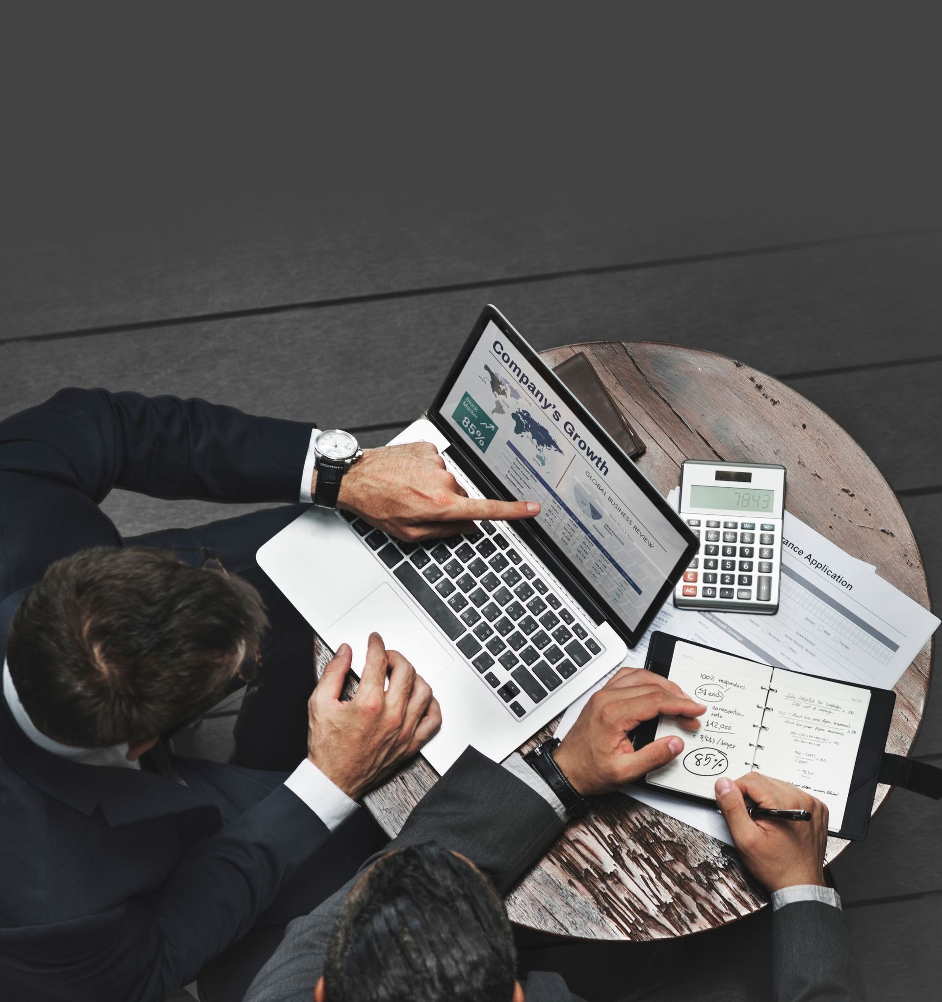 Two men are sitting at a table with a laptop and calculator