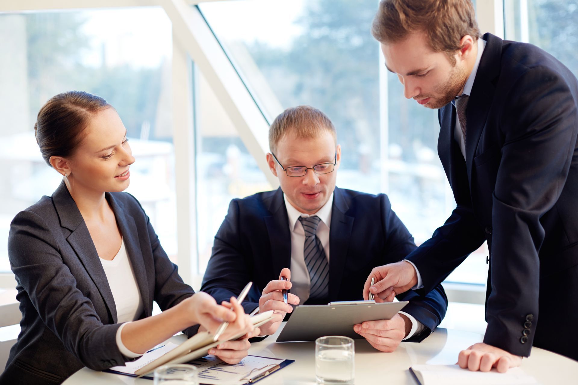 A group of business people are sitting around a table looking at a tablet.