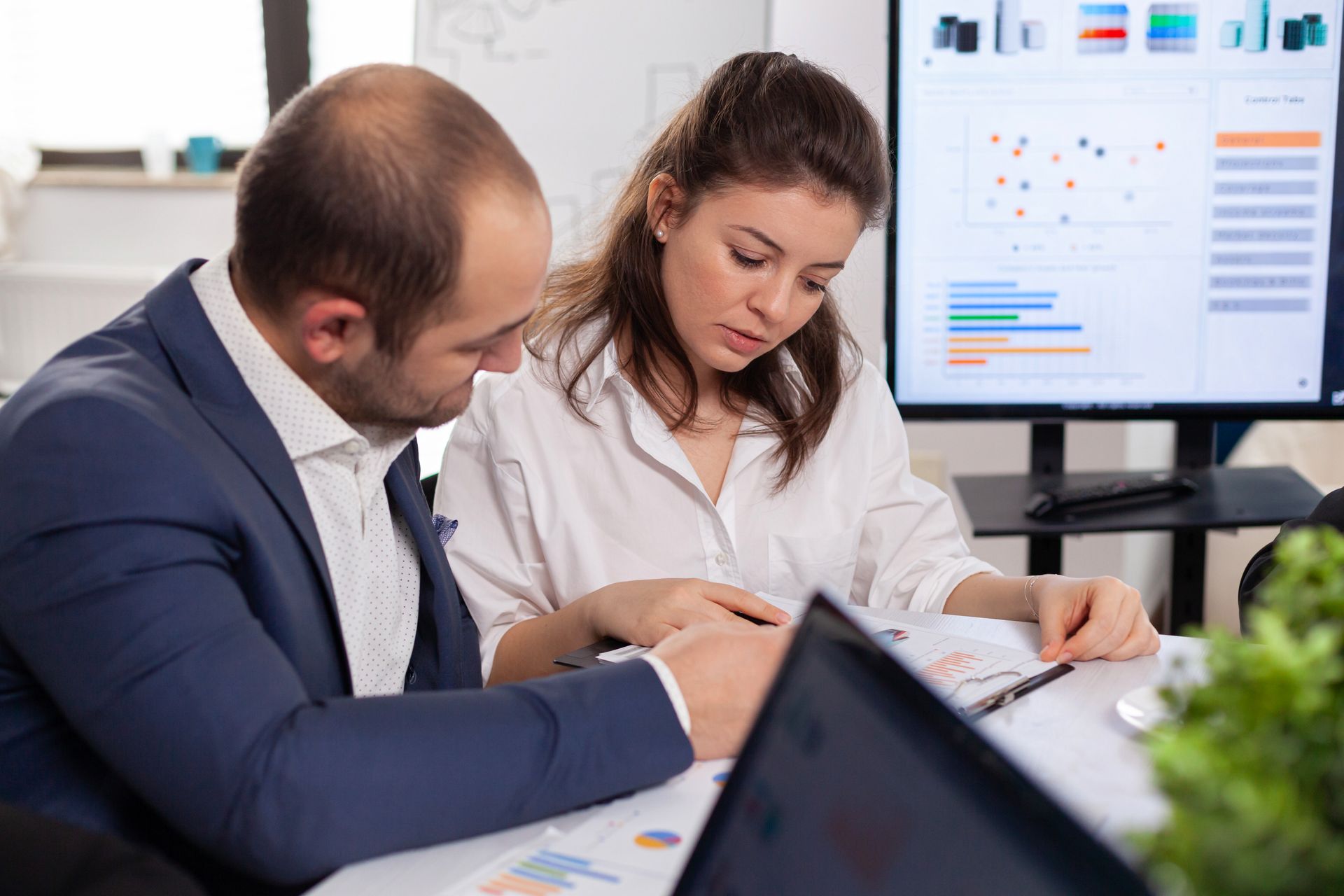 A man and a woman are sitting at a table looking at a laptop.