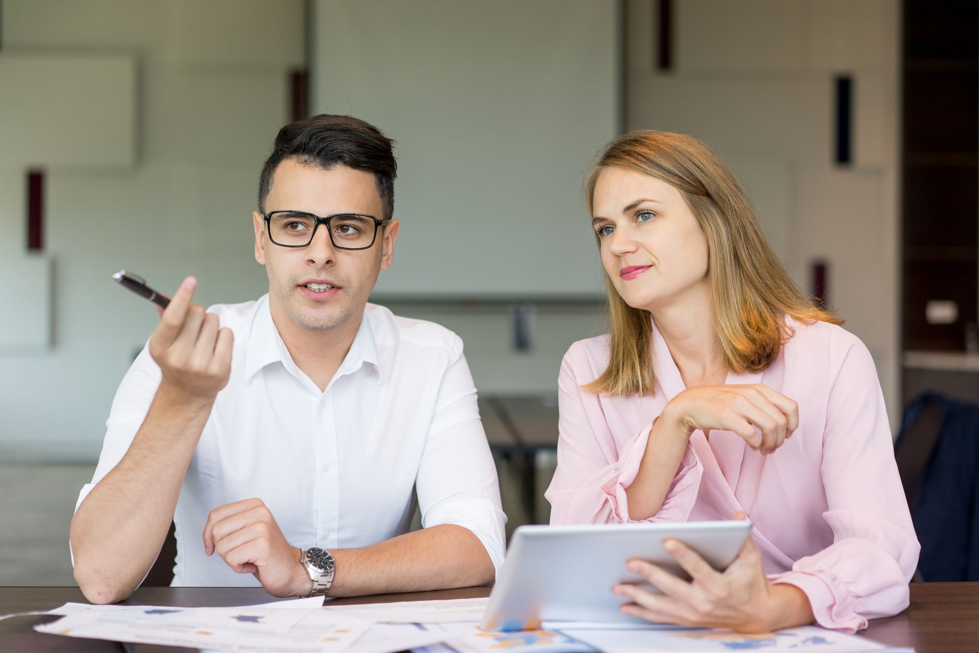 A man and a woman are sitting at a table looking at a tablet.