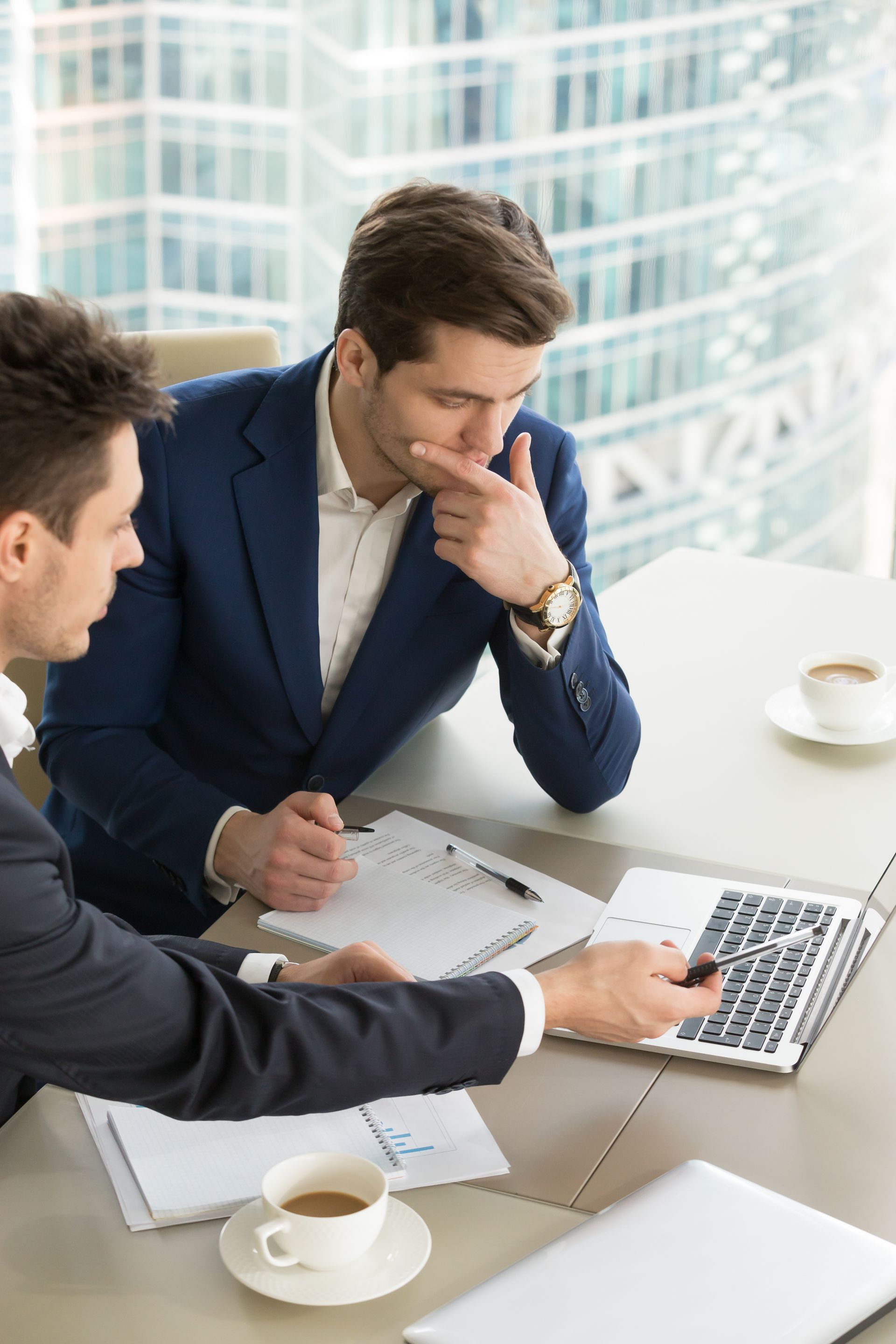 Two men are sitting at a table looking at a laptop computer.