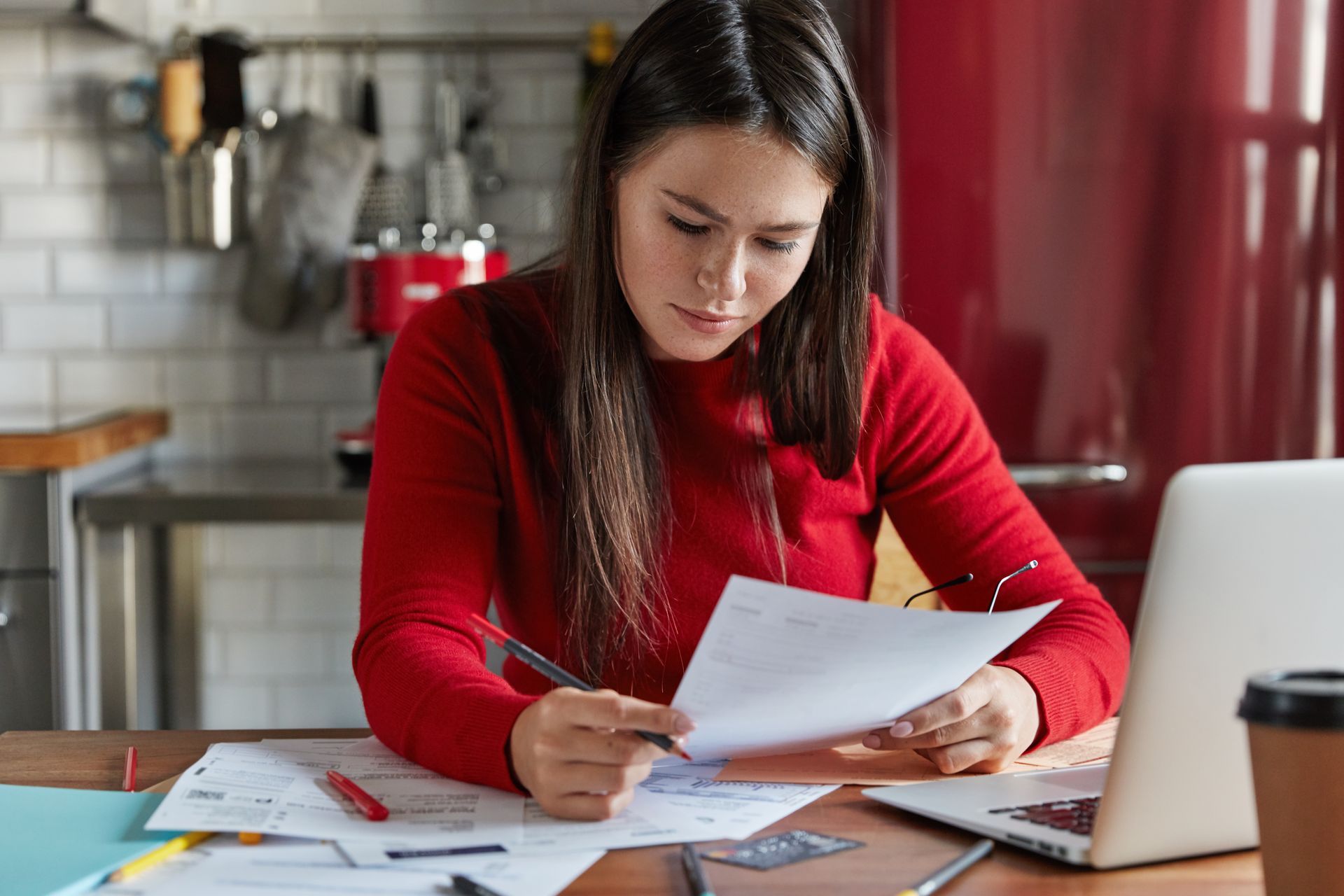 A woman is sitting at a table with a laptop and a piece of paper.