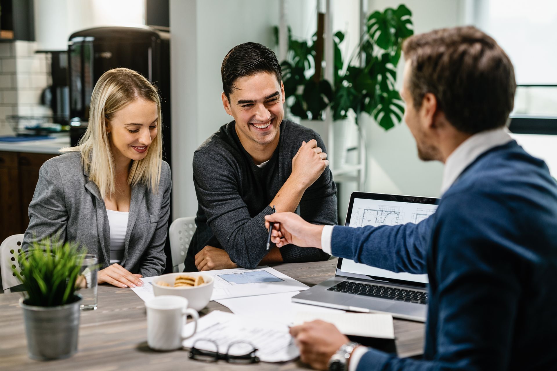 Couple smiling at a financial advisor; discussing documents at a table with a laptop.