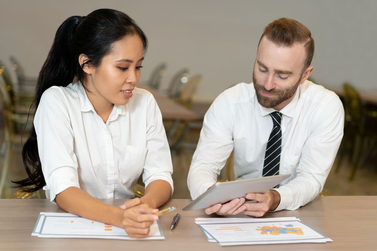 A man and a woman are sitting at a table looking at a tablet.