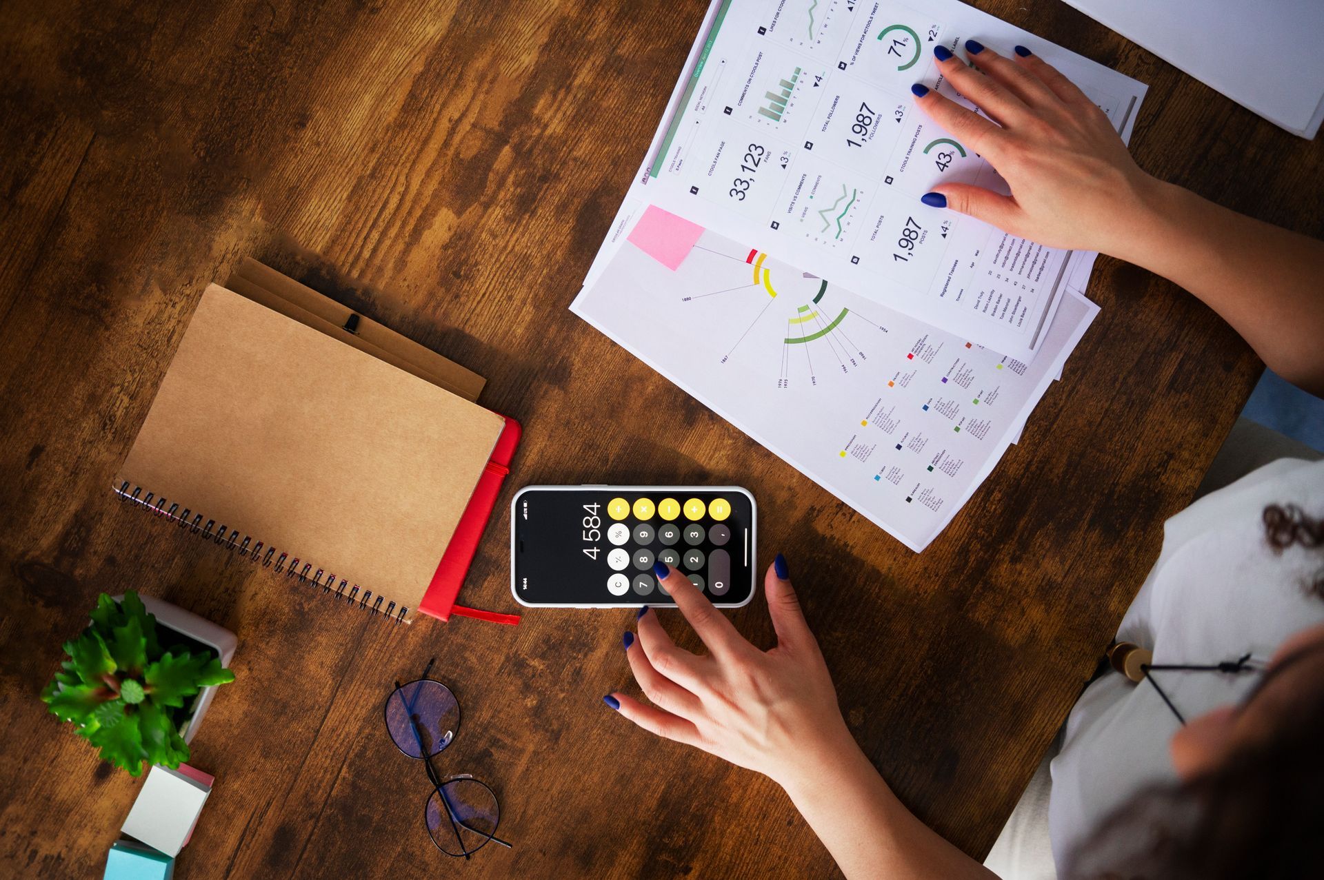 A woman is sitting at a table using a calculator and a cell phone.