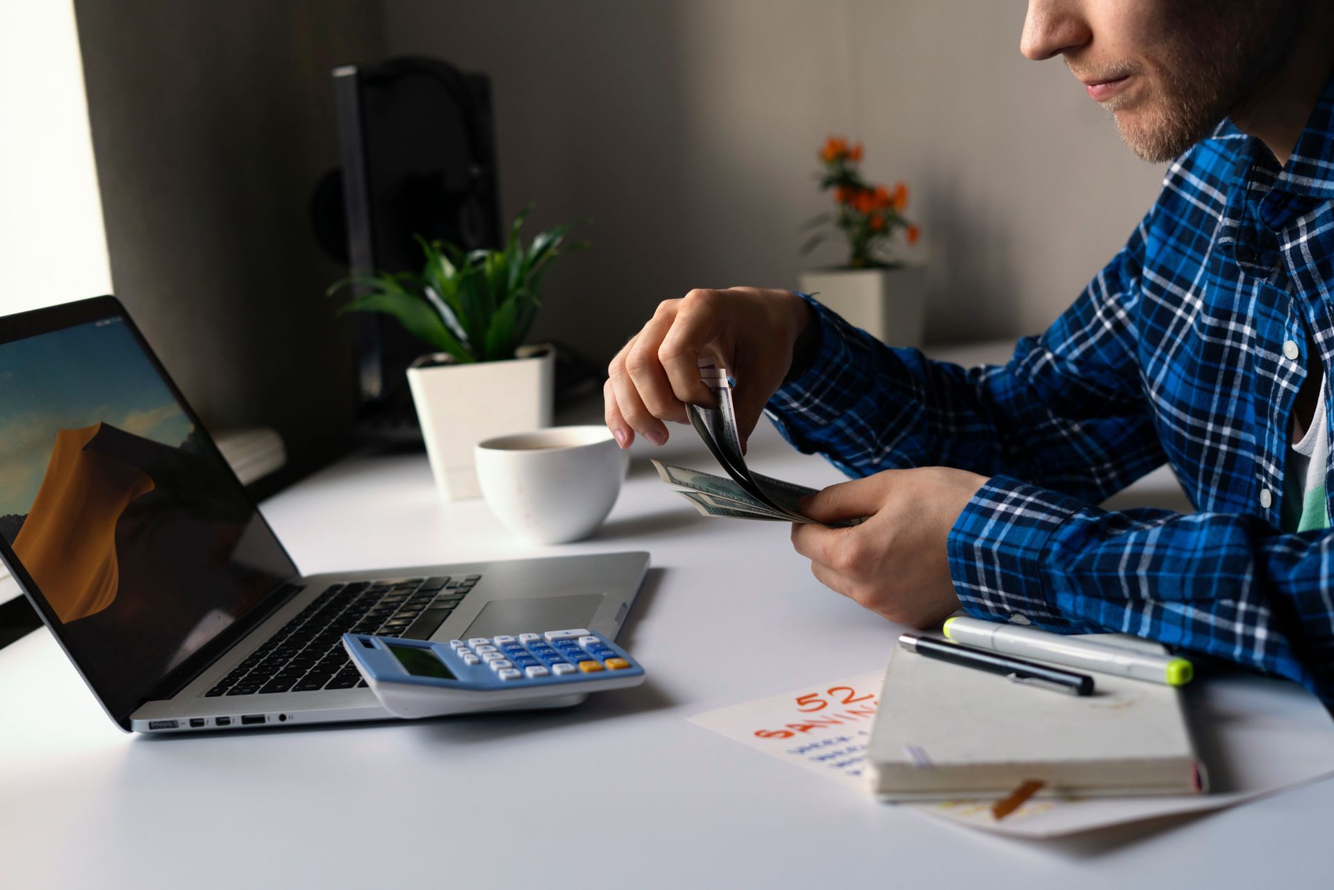 A man is sitting at a desk with a laptop and a cup of coffee.