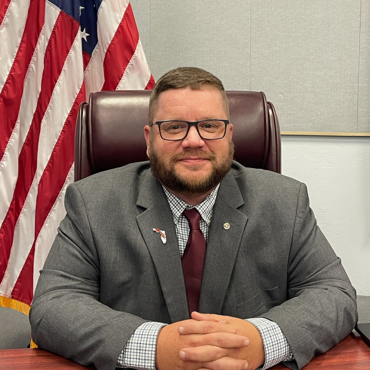 a man in a suit and tie is sitting at a desk in front of an american flag .