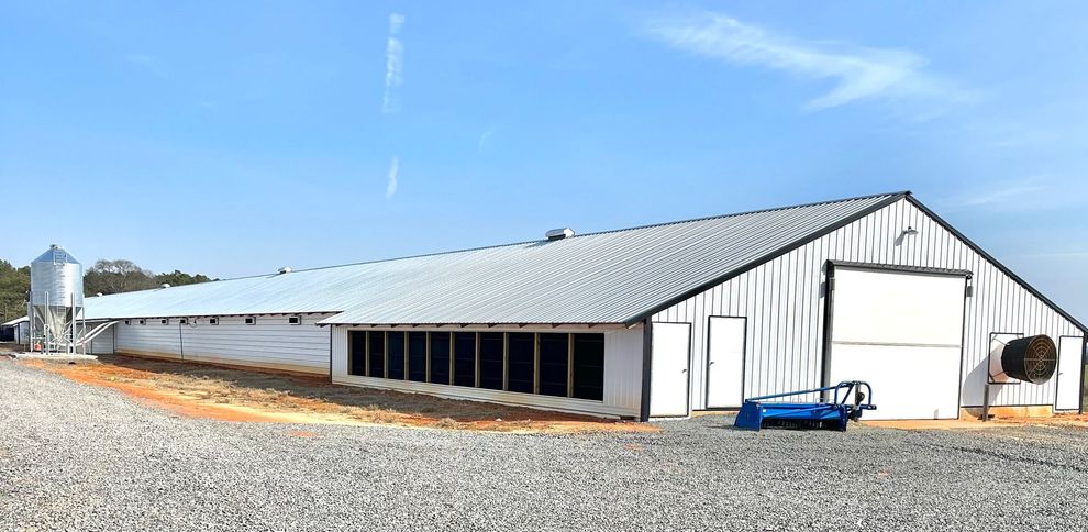 A large white barn is sitting on top of a gravel road.