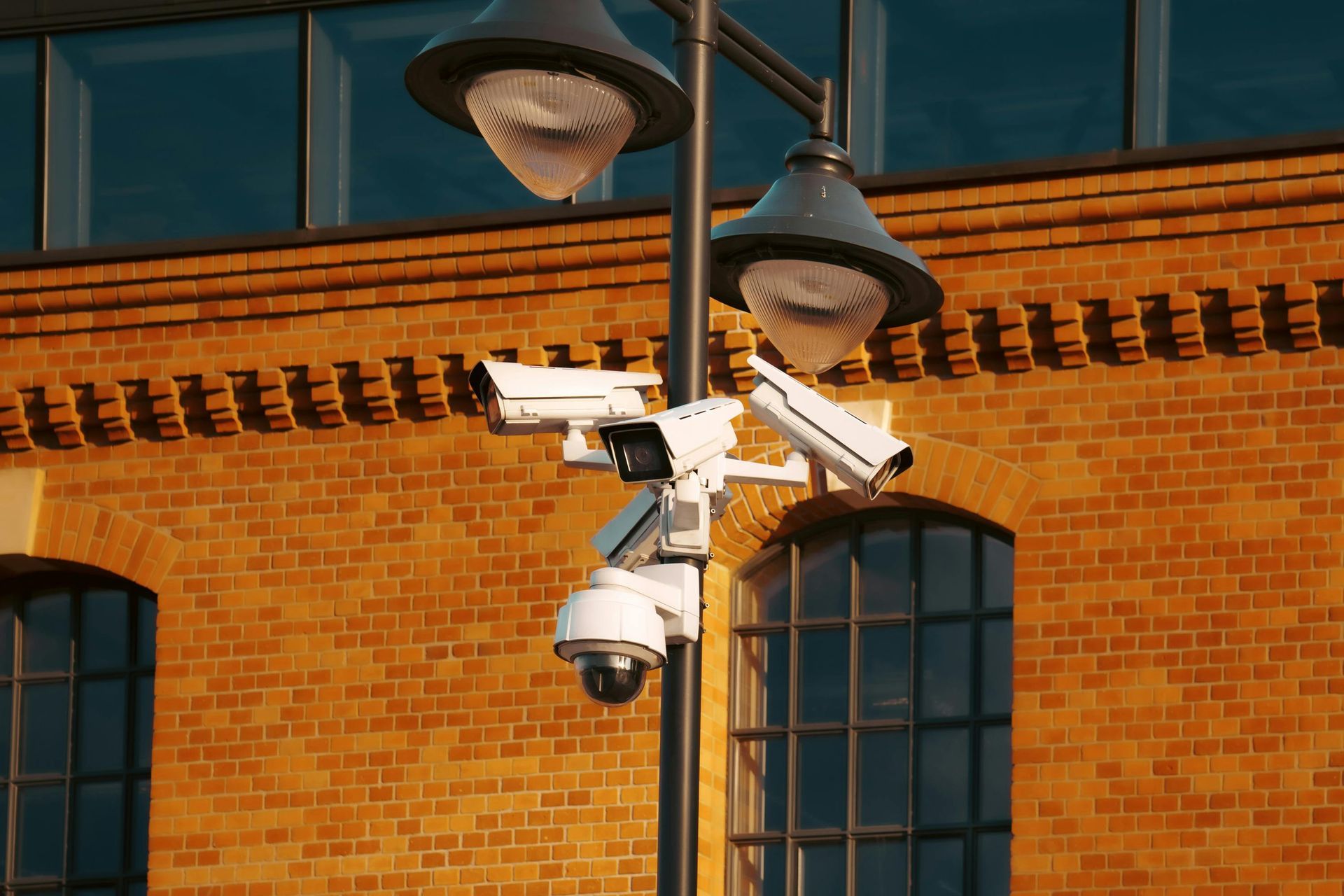 Two security cameras are mounted on a pole in front of a brick building.