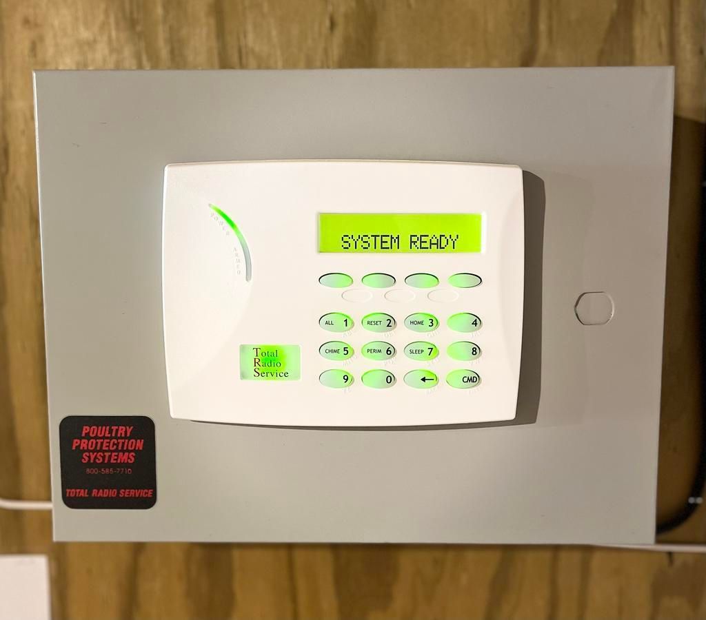 Security system control panel with green lit buttons and display, labeled 