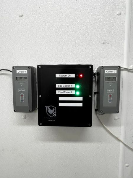 A black box with three lights on it is hanging on a white wall.