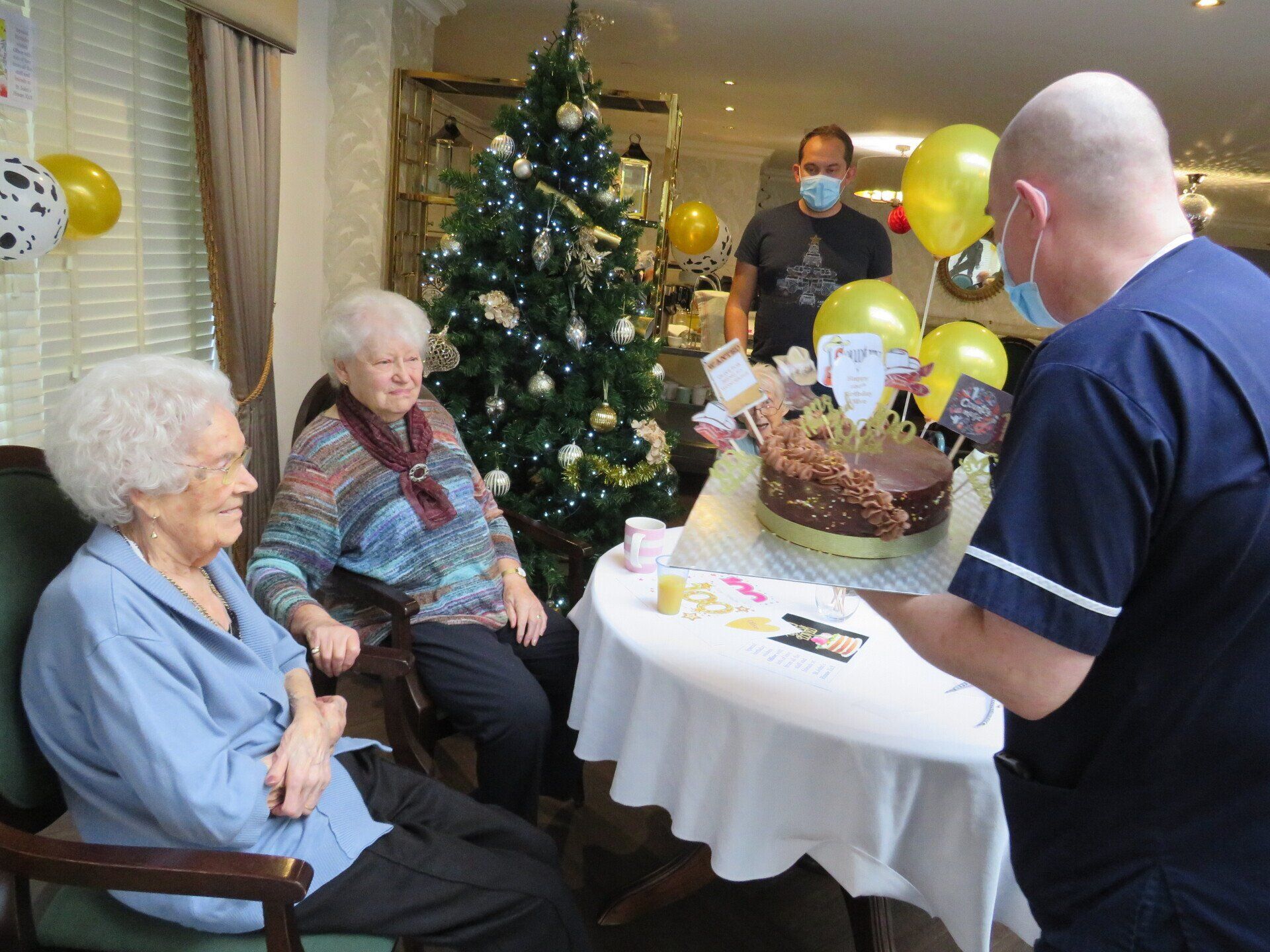 A group of elderly people are sitting around a table with a cake on it