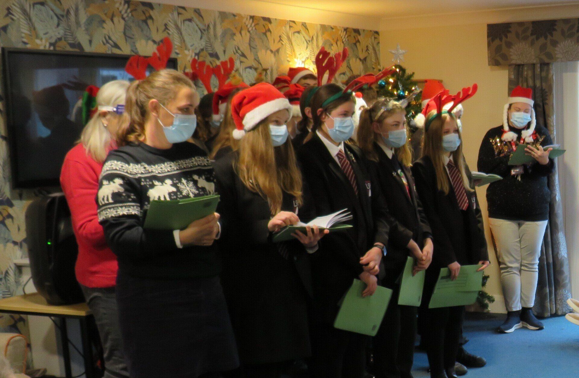 A group of people wearing face masks are singing christmas carols