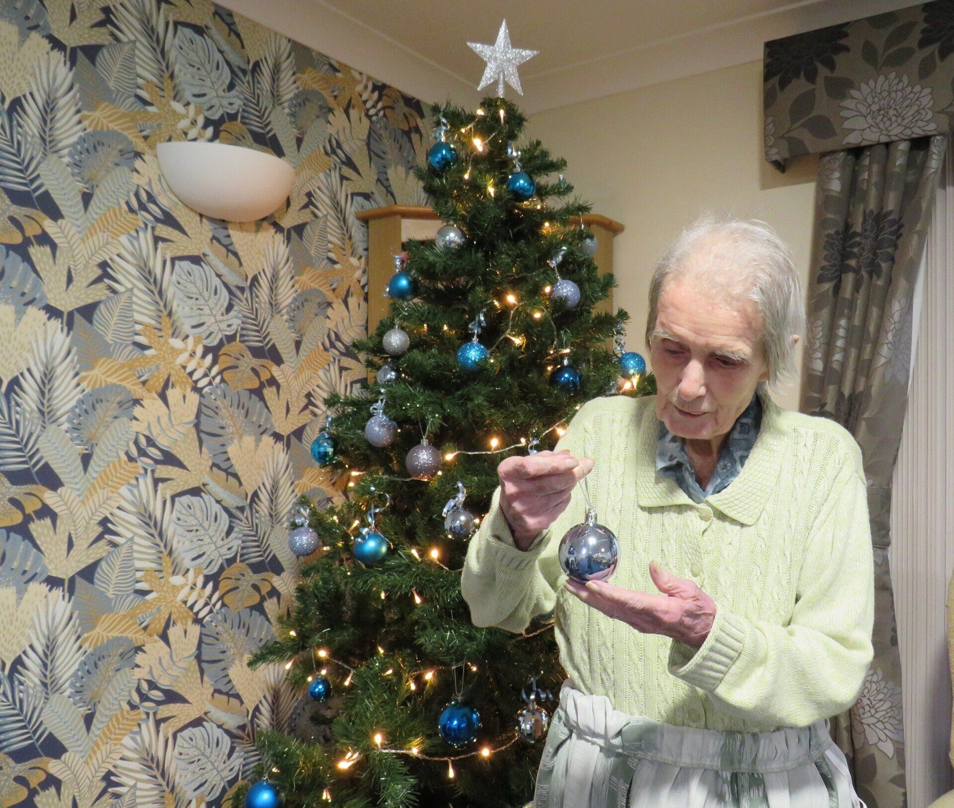 An elderly woman decorates a christmas tree with a star on top