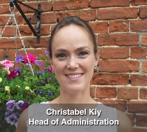 Christabel kiy head of administration is smiling in front of a brick wall