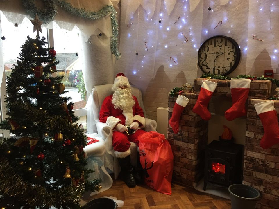 Man dressed as Santa sitting in a chair in the corner of a decorated room