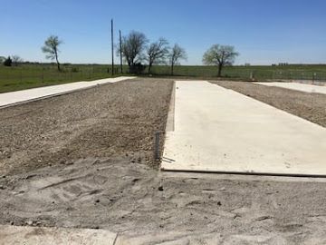 Concrete pads and gravel strips arranged in rows in an open, grassy rural field under a clear blue sky.