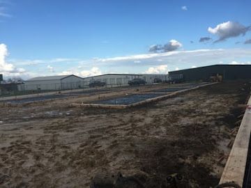 A construction site with concrete foundation pads prepared on a dirt lot under a bright blue sky.