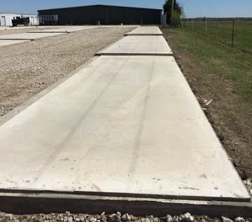 A series of narrow, rectangular concrete pads lined up in a gravel lot next to a large dark building.