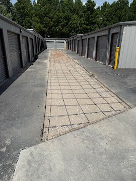 An outdoor storage facility aisle with a central, recessed concrete grid path flanked by asphalt.
