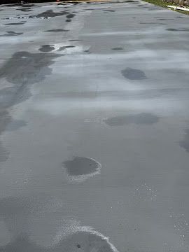 A view of a freshly poured concrete slab with wet patches and varying shades of gray throughout the surface.